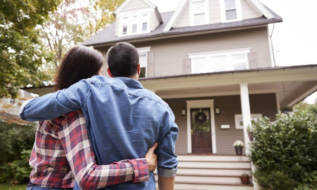 A couple is standing in front of their newly bought home.